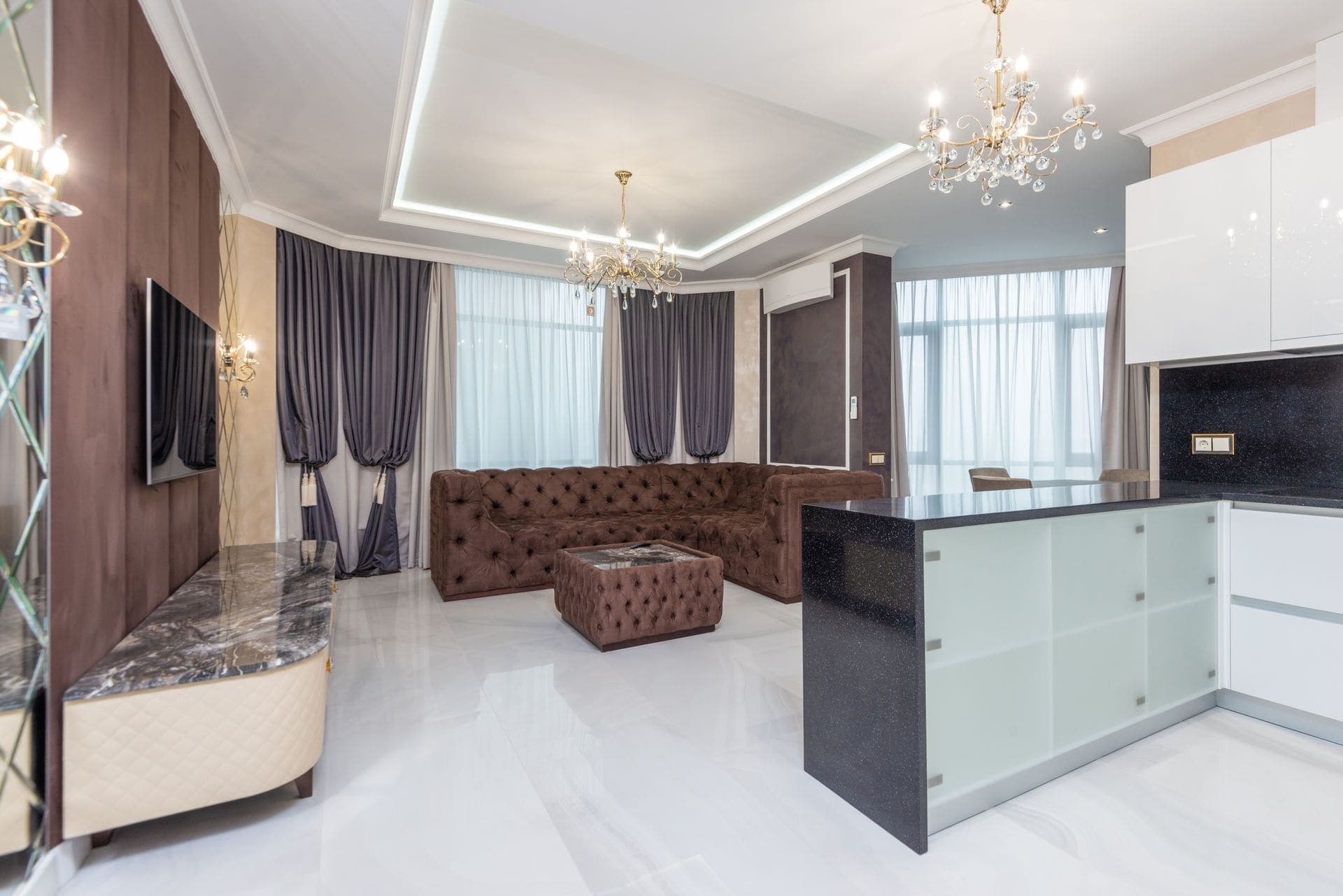 A well-finished modern living room and open kitchen with marble flooring and chandelier lighting